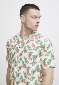 Kurzärmliges Hemd mit Kragen aus leichtem Stoff, mit einem weißen Grund und Mustern aus grünen Blättern und orangenen Flamingos.
