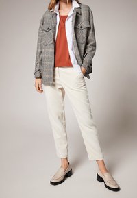 Camicia a quadri grigia, rossa e bianca sopra un top arancione; pantaloni in corduroy crema; mocassini beige con suola nera.