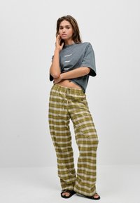 Grijze oversized t-shirt met tekst, olijfgroene geruite wijde broek met verstelbare tailleband en zwarte sandalen. Glad materiaal met een relaxte pasvorm.