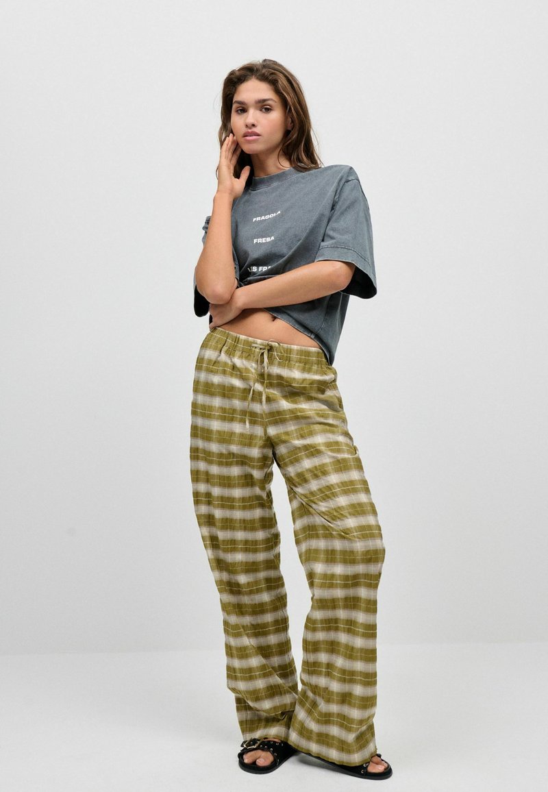 Grijze oversized t-shirt met tekst, olijfgroene geruite wijde broek met verstelbare tailleband en zwarte sandalen. Glad materiaal met een relaxte pasvorm.