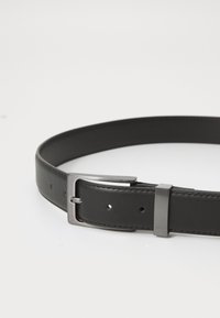 Cinturón de cuero negro con una elegante hebilla de metal plateado y cinco agujeros de ajuste, con una textura suave y un diseño minimalista.