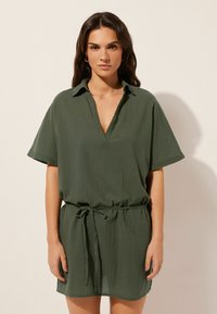 Vestido verde de manga corta con escote en V y cuello, hecho de tejido ligero. Presenta una cintura con cordón y un corte holgado.