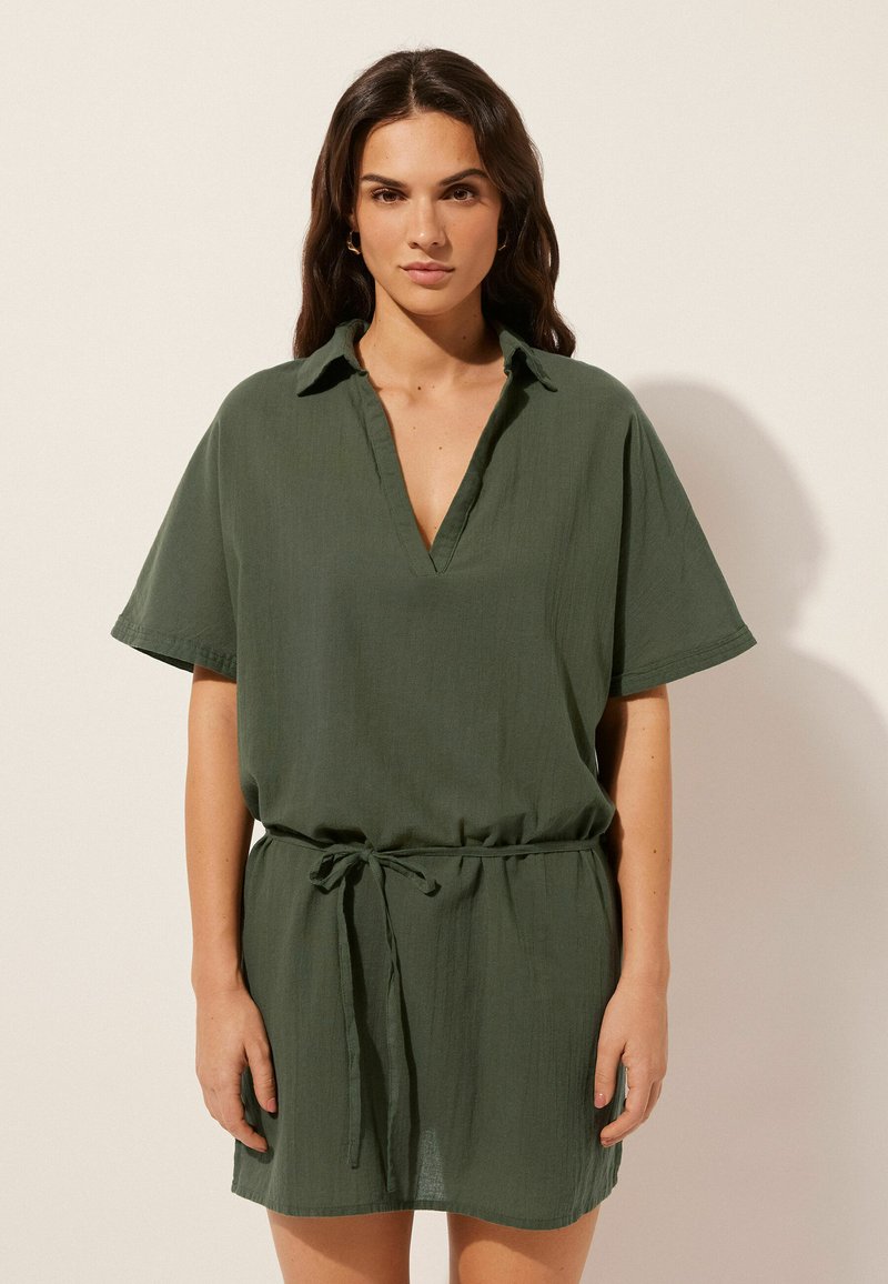 Vestido verde de manga corta con escote en V y cuello, hecho de tejido ligero. Presenta una cintura con cordón y un corte holgado.