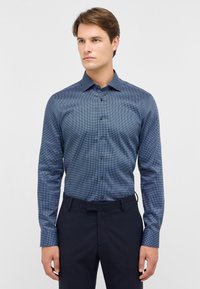 Blau gemustertes Hemd mit Knöpfen, Kragen und langen Ärmeln. Verfügt über ein geometrisches Design und braune Knöpfe. Kombiniert mit dunklen Hosen.