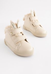 Beige leather baby shoes with plush accents, velcro straps, and rabbit ear details. Round rubber soles with ribbed texture.