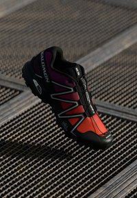 Salomon bėgimo trail batai su juoda, raudona ir purpurine spalvų schema, turintys tekstūruotą padą, patikimą raištelių sistemą ir sustiprintą pirštą.