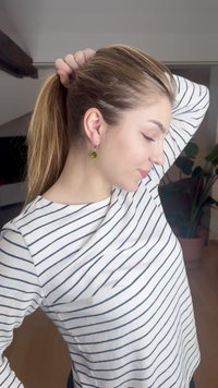 Kvinnelig figur iført en hvit stripete skjorte, med langt hår i hestehale. Hun har grønne dråpeformede øredobber og befinner seg i et hjemmemiljø.