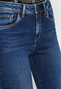 Mörkblå denimjeans med standard femfickorsdesign, kontrasterande sömmar och en säker knäppning i midjan.