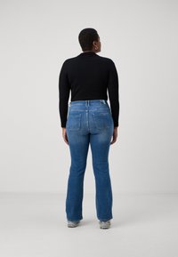 Musta pitkähihainen paita yhdistettynä sinisiin leveälahkeisiin farkkuihin. Farkuissa on kaksi takataskua ja hieman haalistumista. Mallilla on yllään harmaat lenkkarit.