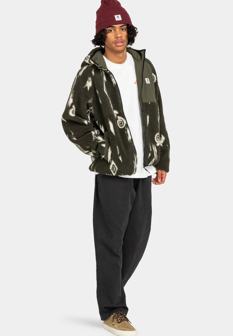 Giacca di felpa verde e bianca con un design a fantasia; presenta una zip frontale, due tasche e un pannello grigio a contrasto. Abbinata a pantaloni scuri.