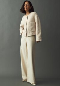 Textured cream jacket with front buttons and patch pocket, paired with wide-leg cream trousers. Both garments have a relaxed fit.