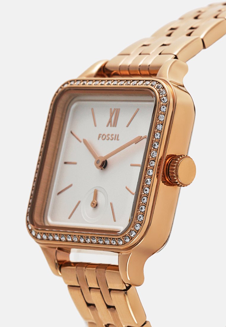 Roségoldene Fossil-Armbanduhr mit quadratischem Ziffernblatt, kristallbesetzter Lünette, weißem Zifferblatt, minimalen Stundenmarkierungen und angeschlossenem Metallarmband.