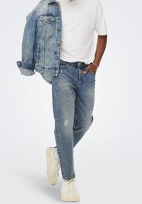 Vaaleansininen farkkutakki, rintataskut ja napitettu; alla valkoinen t-paita; kulutetut vaaleansiniset farkut; paksupohjaiset valkoiset tennarit.