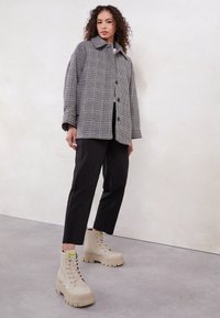 Giacca oversize a scacchi grigi con colletto, pantaloni neri sartoriali e scarponcini beige con lacci e suola texturizzata.