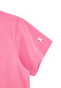 Camiseta de algodón rosa con manga corta. Presenta un logo blanco en la manga izquierda y una textura suave y agradable.