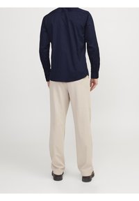 Camisa de manga larga azul marino con una textura sutil, puños abotonados y dobladillo curvado, combinada con pantalones anchos color beige claro y zapatos oscuros.