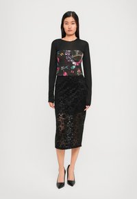 Black long-sleeve top with floral print, paired with a black lace skirt. The outfit features a fitted silhouette and sleek black heels.