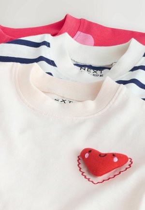 Three t-shirts: pink, white with navy stripes, and white with a red heart patch. Soft cotton fabric, crew neck, casual design, various colors.