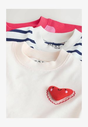 Trzy t-shirty: różowy, biały w granatowe paski oraz biały z czerwoną łatą w kształcie serca. Miękka bawełniana tkanina, dekolt okrągły, casualowy design, różnorodne kolory.