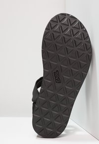 Černá podrážka sandálů Teva s texturovaným trojúhelníkovým vzorem. Obsahuje obdélníkové logo a robustní pásky viditelné po stranách podrážky.