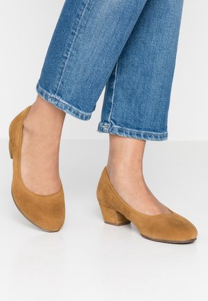 Beige Wildleder-Schuhe mit niedrigem Absatz, abgerundeter Spitze, dezenten Nähten und strukturierter Oberfläche, getragen zu gekürzten blauen Jeans.