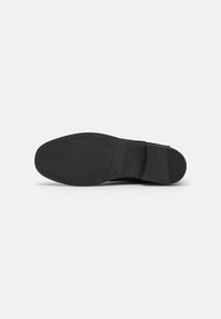 Semelle de chaussure en cuir noir avec grip texturé, de la marque « Tommy Hilfiger », taille 37, présentée sur un fond blanc uni.