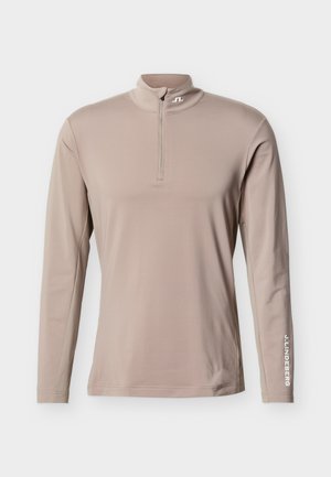 Bež športna majica z dolgimi rokavi, četrtinskim zadrgo, visokim ovratnikom in napisom "J.LINDEBERG" na levem rokuavu.