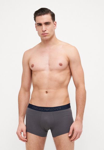 Boxers en coton gris avec une ceinture bleu marine portant le logo "Emporio Armani" en lettres bleu clair, design ajusté.