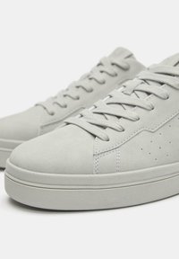 Hellgraue Sneakers aus Wildleder mit flachen Schnürsenkeln, minimalistischem Design und perforierten Akzenten an den Seiten. Dicke Gummisohle.