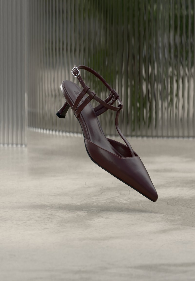 Escarpin slingback en cuir brun foncé à bout pointu, avec des fines lanières et un petit talon kitten incurvé, présenté sur un fond abstrait.