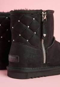 Svarta ankelboots i mocka med quiltat mönster, silvernitar och dragkedja på sidan. Mjuk foder av päls och en texturerad sula.
