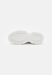 Suela de zapatilla blanca con una superficie texturizada, que presenta un patrón acanalado y zonas planas para mayor agarre. Construcción de goma gruesa y duradera.