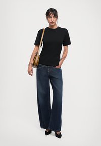 Black short-sleeve t-shirt paired with wide-leg dark denim jeans. Accessorized with a tan crossbody bag and black pointed-toe heels.