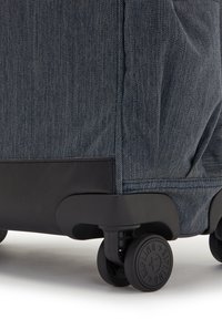Valigia in denim scuro con una base nera liscia, dotata di quattro ruote nere e dettagli di cucitura visibili lungo il tessuto.