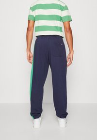 Bomullsmix-outfit som består av en grön och vit randig kortärmad skjorta, matchad med marinblå byxor och en grön sidopanel.