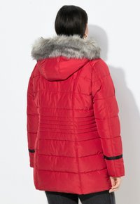 Giacca piumino rossa con cappuccio rifinito in pelliccia sintetica, trapuntatura a canale e polsini elasticizzati. Caratterizzata da una vestibilità slim e una texture liscia e lucida.