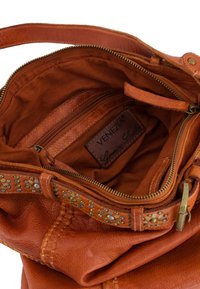 Leren handtas in roestoranje met een gestructureerd oppervlak. Heeft een binnenzak met rits en decoratieve metalen accenten langs de opening.