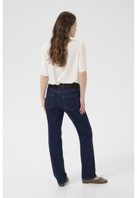 Blouse blanche ajustée à manches courtes, assortie à un jean en denim bleu foncé. Le jean possède des poches arrière et un design à jambe droite. Ballerines en daim.