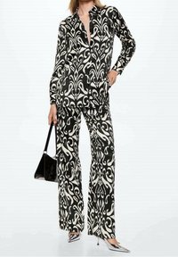 Set composto da camicia a righe bianche e nere e pantaloni a gamba larga, caratterizzato da un design astratto, tessuto morbido e texture liscia. Accompagnato da una borsa nera.