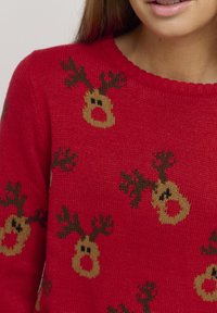 Pull en tricot rouge avec un motif de renne récurrent en marron et beige, doté un col côtelé et d'une texture lisse.