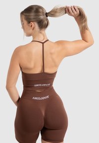 Bruin naadloze twee-delige activewear set met een cropped top en hoog ingezette shorts, met minimale branding op de achterkant.