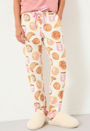 Weiße Schlafanzughosen mit einem bunten Druck von Donuts, Gebäck und Gläsern, ausgestattet mit einem pinken Kordelzug, kombiniert mit flauschigen weißen Hausschuhen.