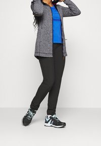 Giacca grigia a maglia con zip, t-shirt blu, pantaloni neri e scarpe da ginnastica nere con accenti blu chiaro. Un outfit adatto per l'abbigliamento sportivo.