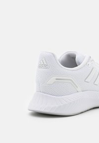 Bílá sportovní obuv s mesh svrškem, strukturovaným povrchem, polstrovaným límcem a gumovou podrážkou. Obsahuje logo Adidas ve stříbrné barvě.