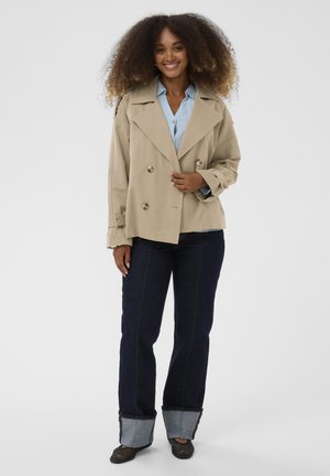 Trenci bej cu două rânduri de nasturi, reveruri mari, purtat peste o cămașă albastru deschis. Blugi albastru închis cu accente albastru deschis la manșete, pantofi negri.