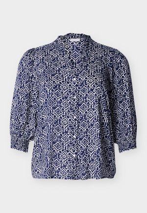 Blouse bleu marine avec un motif floral géométrique blanc, devant boutonné, manches trois-quarts avec poignets élastiques, et col mao.