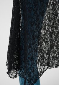 Tissu en dentelle florale noire drapé sur un jean en denim bleu, mettant en évidence le contraste entre la dentelle délicate et la texture robuste du denim.
