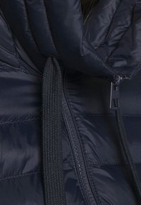 Giacca imbottita blu navy con collo alto, dotata di cerniera e coulisse. Tessuto strutturato con sezioni trapuntate per l'isolamento.