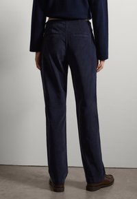 Pantalons en velours côtelé bleu marine avec des jambes droites, deux poches arrière et une texture lisse. Portés avec un pull sombre et des chaussures brunes.
