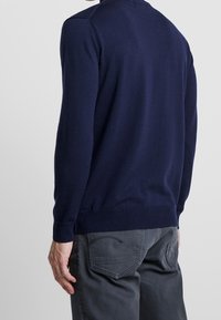 Námorně modrý pletený svetr s kulatým výstřihem a žebrovanými manžetami. Hladká textura, přiléhavý střih. V kombinaci s tmavě šedými kalhotami se zadními kapsami.